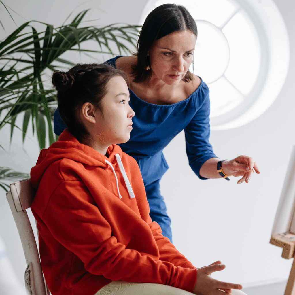 Lead Out Loud youth sitting in a chair as a teacher stands and assists the youth with their work.